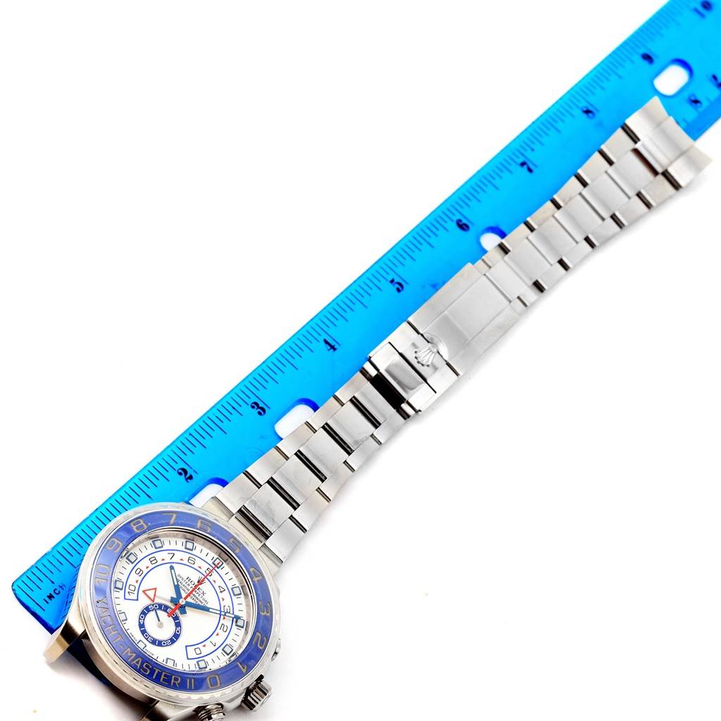 The Rolex Yacht-Master 116680 Men's Stainless Steel White Dial 116680 Men's Stainless Steel White Dial watch is shown from a top-down angle with its metal bracelet extended next to a blue ruler.