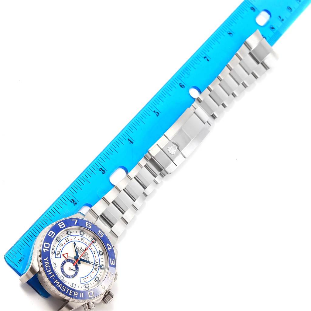 The Rolex Yacht-Master 116680 Men's Stainless Steel White Dial 116680 Men's Stainless Steel White Dial watch is shown from a top-down angle with its bracelet and clasp extended, alongside a blue ruler.