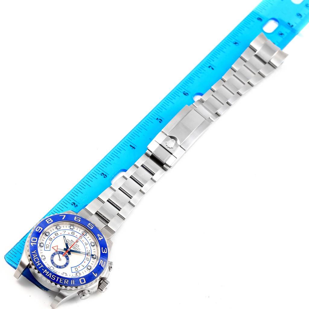 The image shows the Yacht-Master model by Rolex, displaying the watch dial, bezel, and bracelet laid flat alongside a blue ruler.