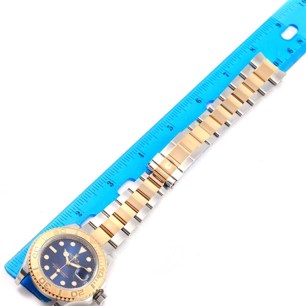 The Rolex Yacht-Master 16623 Men's Stainless Steel Blue Dial 16623 Men's Stainless Steel Blue Dial watch is shown from an overhead angle, displaying its face, bezel, strap, and partially extended bracelet alongside a ruler.