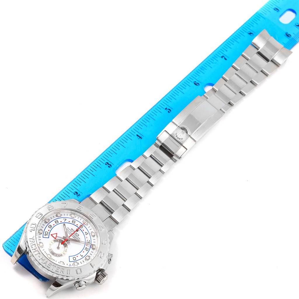 The Rolex Yacht-Master 116689 Men's White Gold White Dial 116689 Men's White Gold White Dial watch is displayed face-up alongside a blue ruler, showcasing the dial and bracelet.