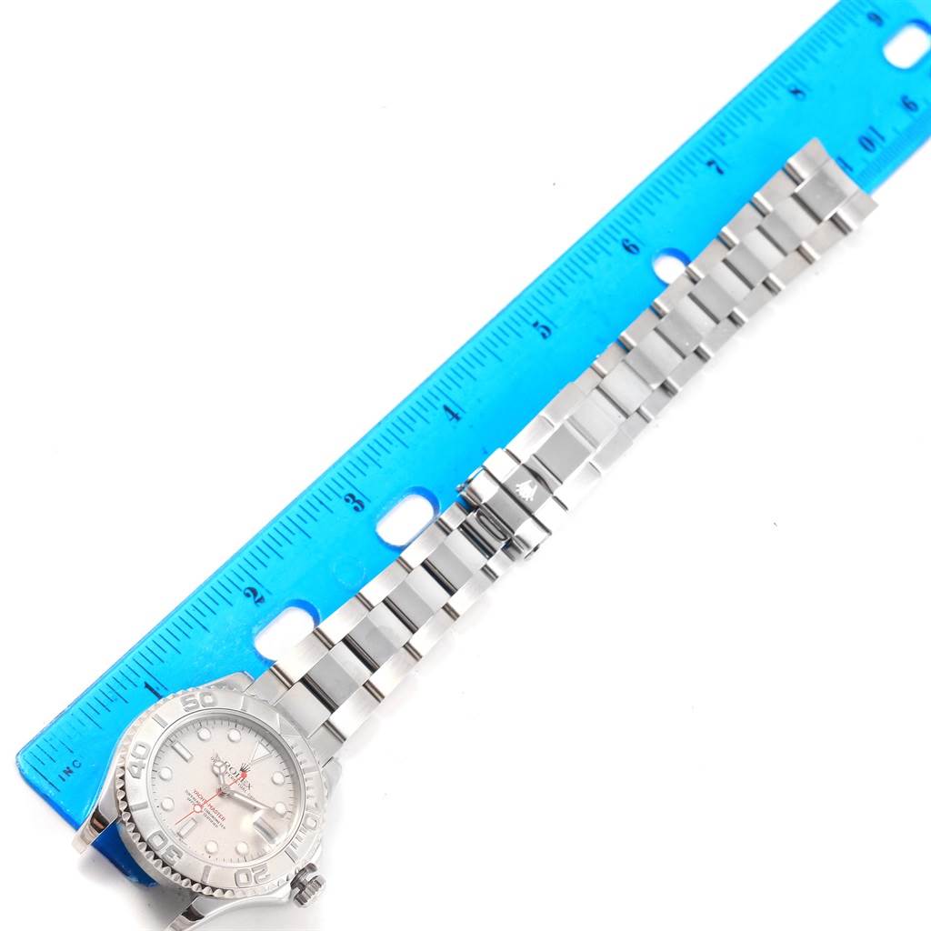 The Rolex Yacht-Master 168622 Men's Stainless Steel Silver Dial 168622 Men's Stainless Steel Silver Dial watch is shown lying flat with its band extended next to a blue ruler for size reference.