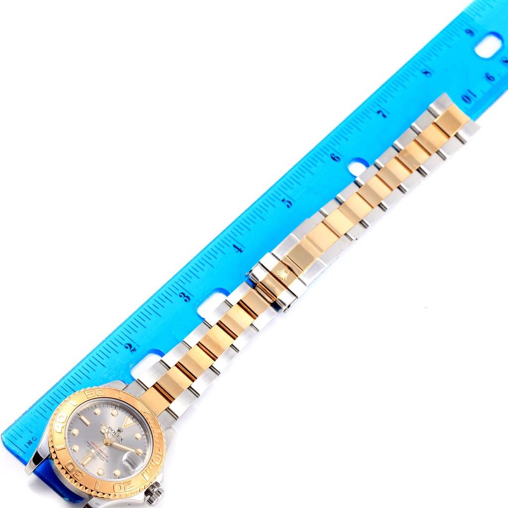 The Rolex Yacht-Master 168623 Men's Steel and Gold (two tone) Grey Dial 168623 Men's Steel and Gold (two tone) Grey Dial watch is shown from top-down, highlighting its face, bezel, and two-tone bracelet beside a blue ruler.