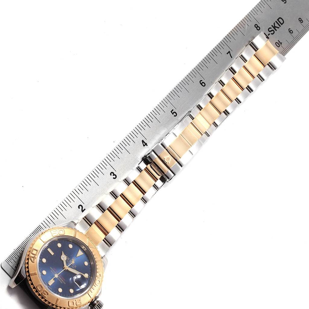This image shows a Rolex Yacht-Master 16623 Men's Stainless Steel Blue Dial 16623 Men's Stainless Steel Blue Dial watch laying flat with focus on its two-tone bracelet and a partial view of the dial and bezel, alongside a ruler for size reference.