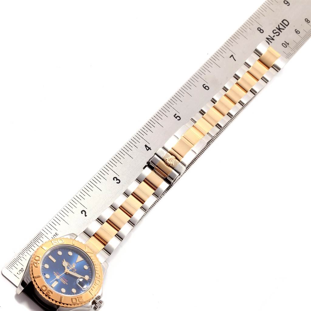 The image shows a Rolex Yacht-Master 168623 Men's Steel and Gold (two tone) Blue Dial 168623 Men's Steel and Gold (two tone) Blue Dial watch lying flat with its metal strap extended alongside a ruler.
