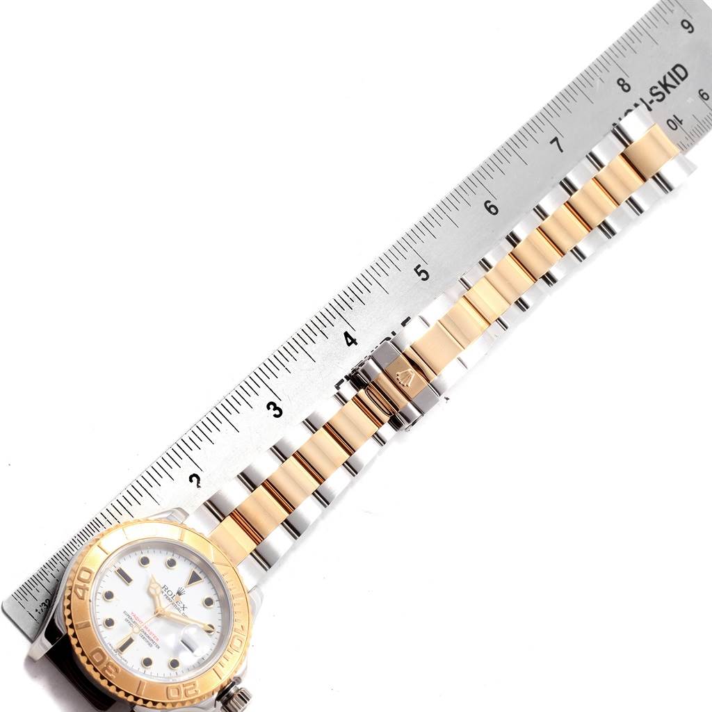 The image shows a side angle of a Rolex Yacht-Master 16623 Men's Stainless Steel White Dial 16623 Men's Stainless Steel White Dial watch with a white dial, gold bezel, and two-tone bracelet next to a ruler.