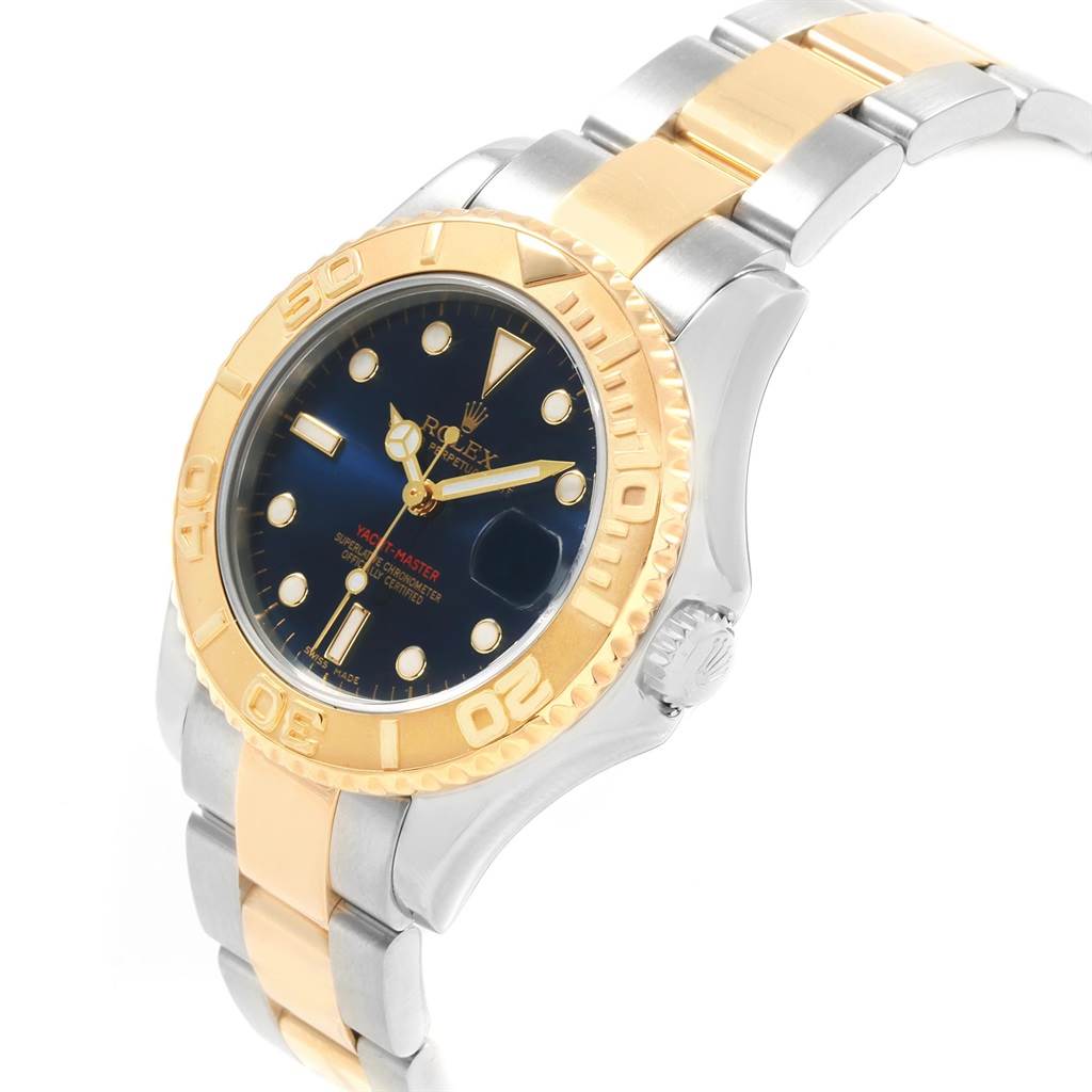 The image shows a Rolex Yacht-Master 168623 Men's Steel and Gold (two tone) Blue Dial 168623 Men's Steel and Gold (two tone) Blue Dial watch at an angle showcasing its blue dial, gold bezel, and two-tone metal bracelet.