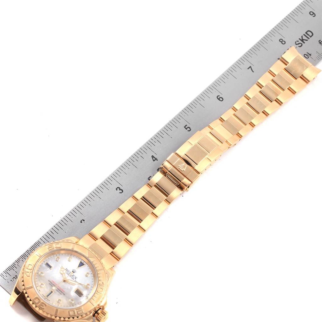 The image shows a Rolex Yacht-Master 16628 Men's Yellow Gold Mother of Pearl Dial 16628 Men's Yellow Gold Mother of Pearl Dial watch with its gold bracelet laid next to a ruler for scale.