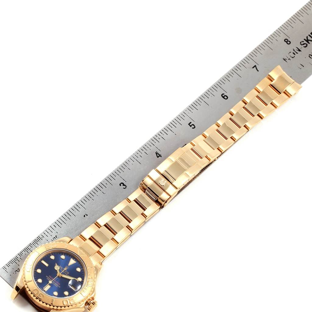 The image shows a top view of a Rolex Yacht-Master 68628 Yellow Gold Blue Dial 68628 Yellow Gold Blue Dial watch, featuring its gold bracelet and blue dial, measured against a ruler.