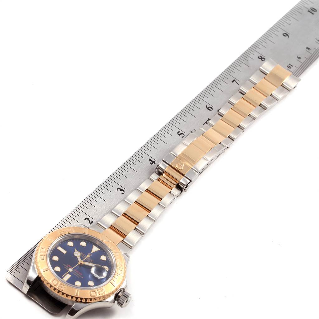 The image shows a top-down view of a Rolex Yacht-Master 16623 Men's Stainless Steel Blue Dial 16623 Men's Stainless Steel Blue Dial watch with a two-tone bracelet next to a ruler.