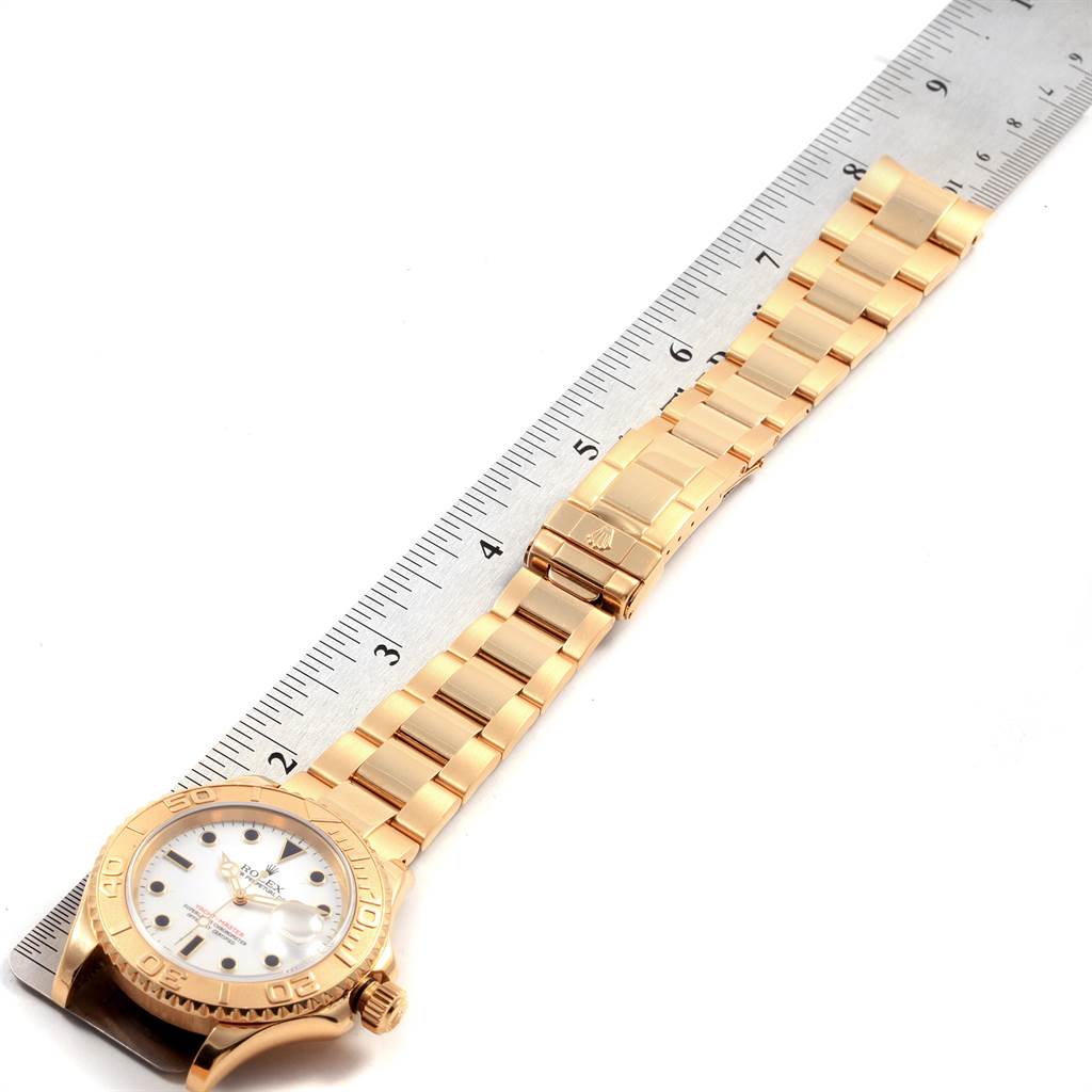 The image shows a Rolex Yacht-Master 16628 Men's Yellow Gold White Dial 16628 Men's Yellow Gold White Dial watch in gold with a ruler for size reference, focusing on the bracelet and dial.