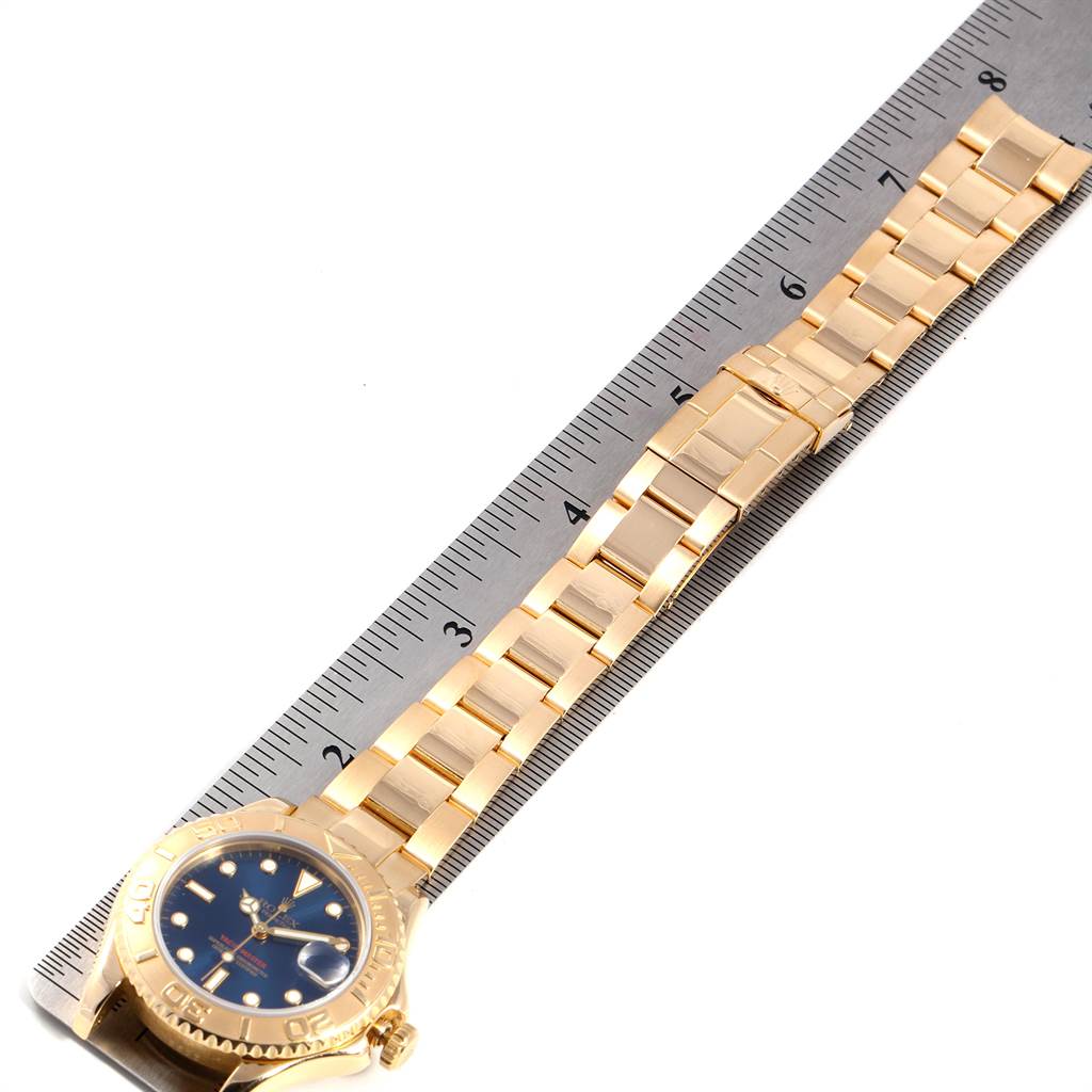 The image shows a side angle of a gold Rolex Yacht-Master 68628 Yellow Gold Blue Dial 68628 Yellow Gold Blue Dial watch, displaying the face, bezel, and bracelet laid on a ruler.