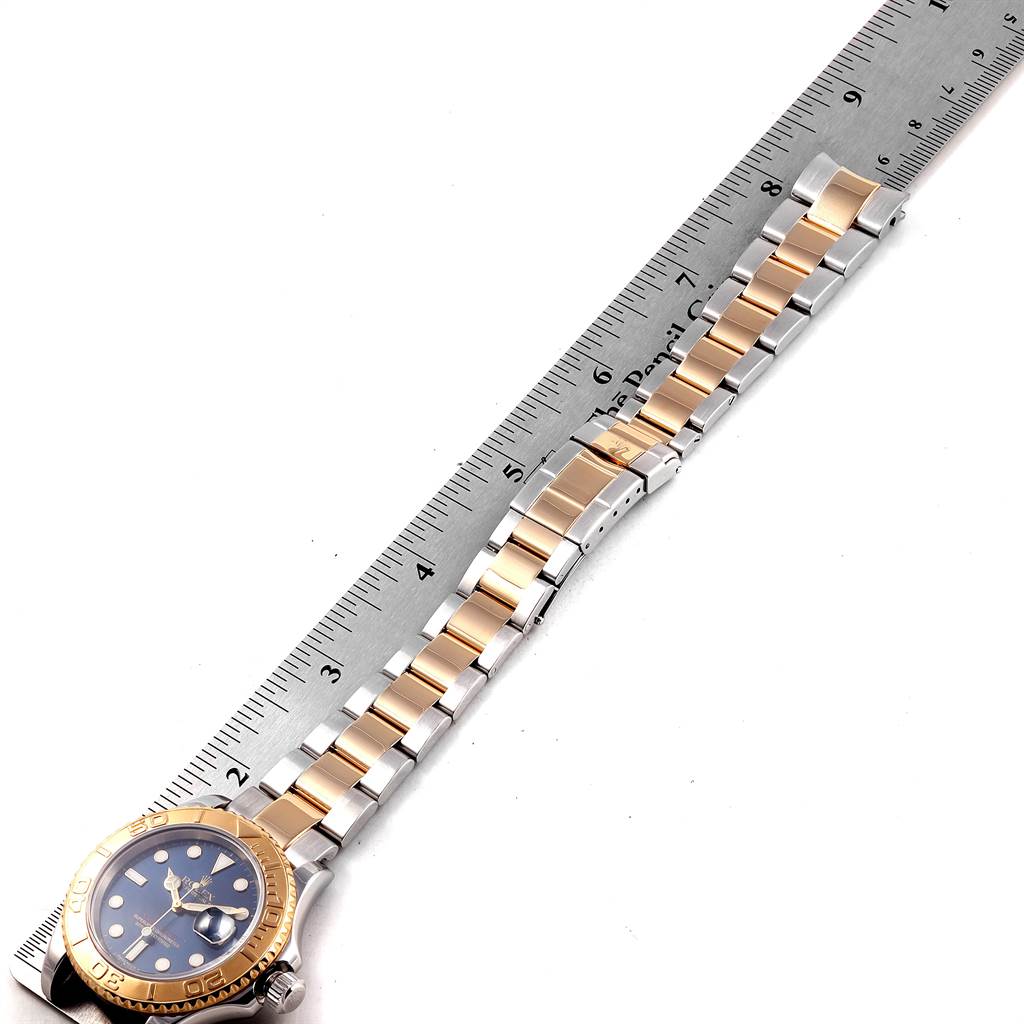 The image shows a Rolex Yacht-Master 16623 Men's Stainless Steel Blue Dial 16623 Men's Stainless Steel Blue Dial watch viewed from above, highlighting its two-tone bracelet and a portion of a metal ruler.