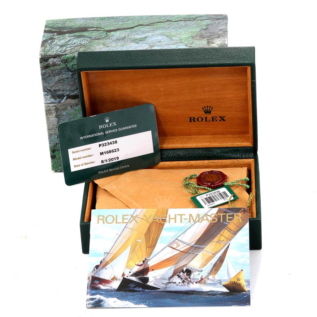 The image shows packaging and accessories for a Rolex Yacht-Master 168623 Men
s Steel and Gold (two tone) Grey Dial 168623 Men
s Steel and Gold (two tone) Grey Dial, including a service guarantee card, booklet, and box.