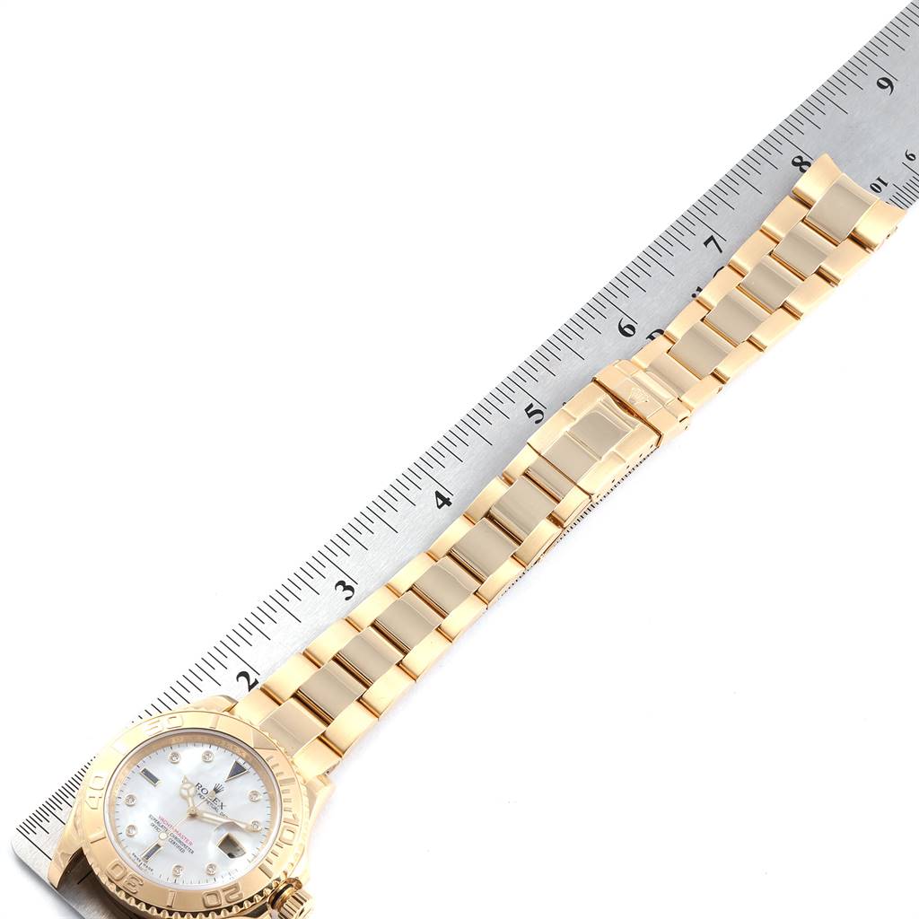 The image shows a Yacht-Master model Rolex watch laid flat, showcasing the dial, bezel, and bracelet next to a ruler for scale.