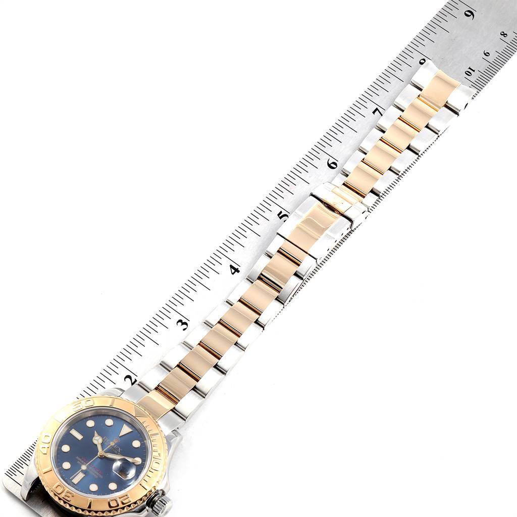 The image shows the Rolex Yacht-Master 16623 Men's Stainless Steel Blue Dial 16623 Men's Stainless Steel Blue Dial watch laid flat with its blue dial, gold bezel, and bracelet against a ruler.