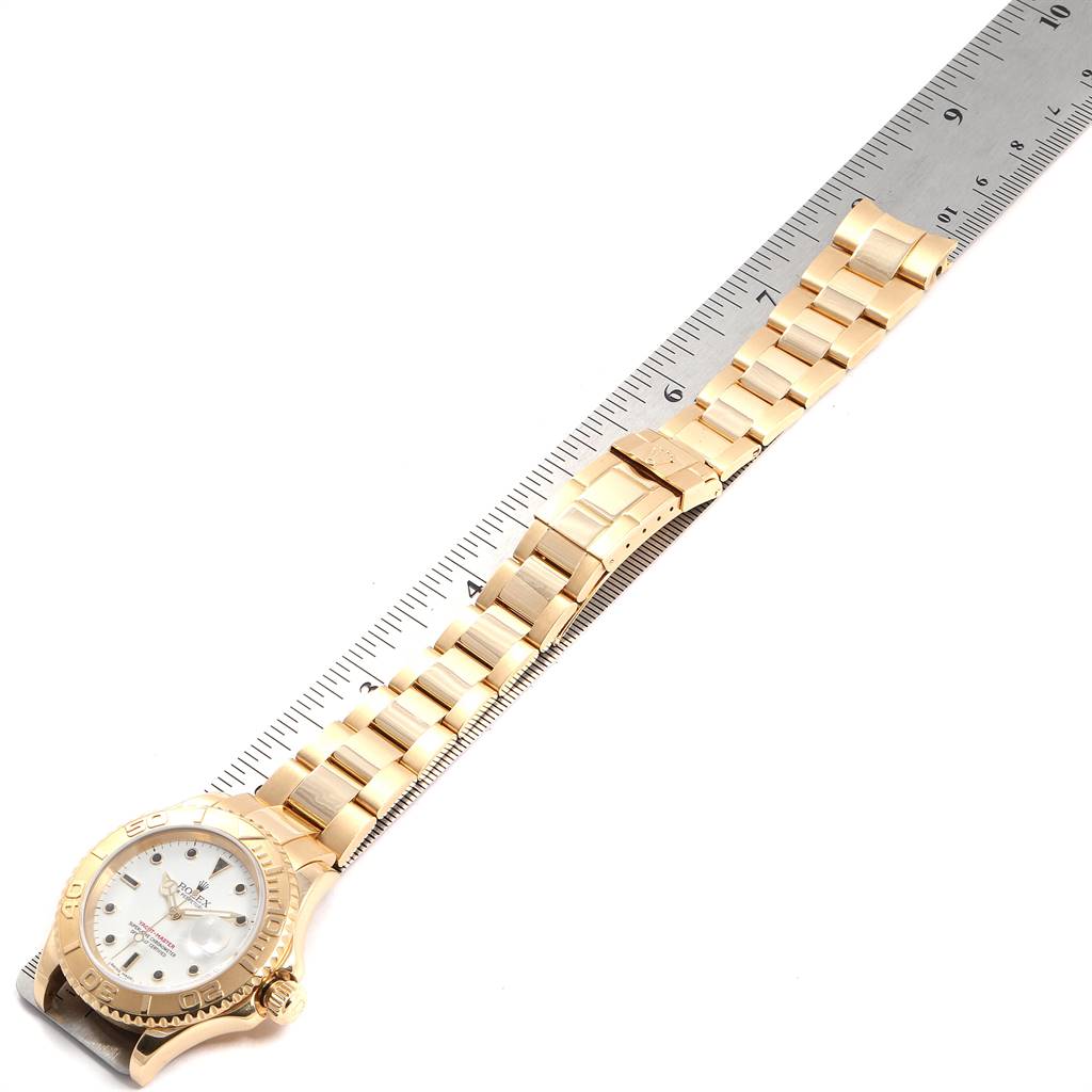 The Rolex Yacht-Master 16628 Men's Yellow Gold White Dial 16628 Men's Yellow Gold White Dial watch is shown from a top-down angle, highlighting its face, bezel, and full metal bracelet next to a ruler.