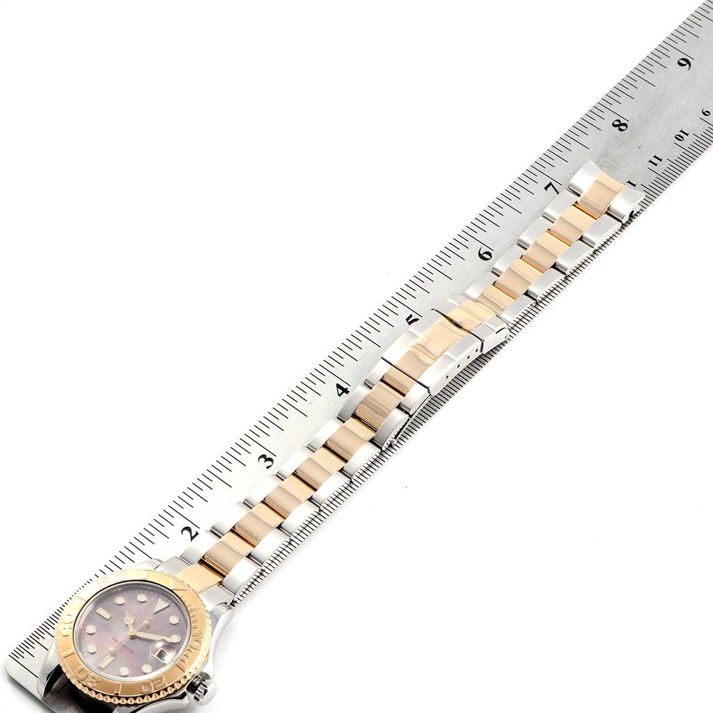The Rolex Yacht-Master 168623 Men
s Steel and Gold (two tone) Mother of Pearl Dial 168623 Men
s Steel and Gold (two tone) Mother of Pearl Dial watch is shown from the top, featuring its face and two-toned metal bracelet alongside a ruler.