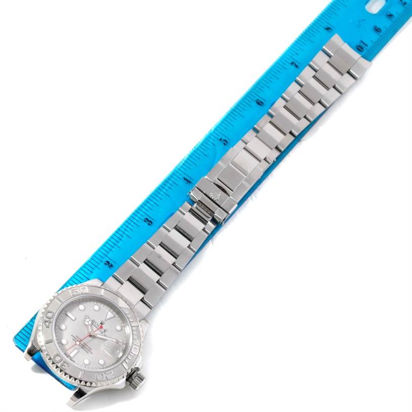 The image shows a top view of a Rolex Yacht-Master 16622 Men's Stainless Steel Silver Dial 16622 Men's Stainless Steel Silver Dial watch with its bracelet extended alongside a blue ruler.