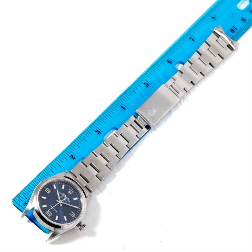 The Rolex Air-King 14000 Men's Stainless Steel Blue Dial 14000 Men's Stainless Steel Blue Dial watch is shown from a top-down angle, featuring the dial, bracelet, and clasp next to a blue ruler.