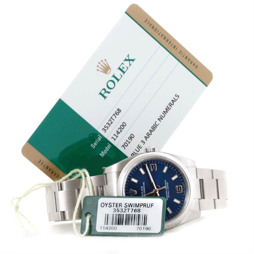 The Rolex Air-King 114200 Men's Stainless Steel Blue Dial 114200 Men's Stainless Steel Blue Dial watch is shown from a slight side angle, along with its warranty card and tags visible.