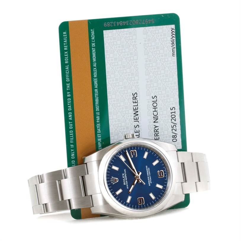 The image shows a Rolex Air-King 114200 Men's Stainless Steel Blue Dial 114200 Men's Stainless Steel Blue Dial watch with a blue dial, partial bracelet, and an accompanying green warranty card.