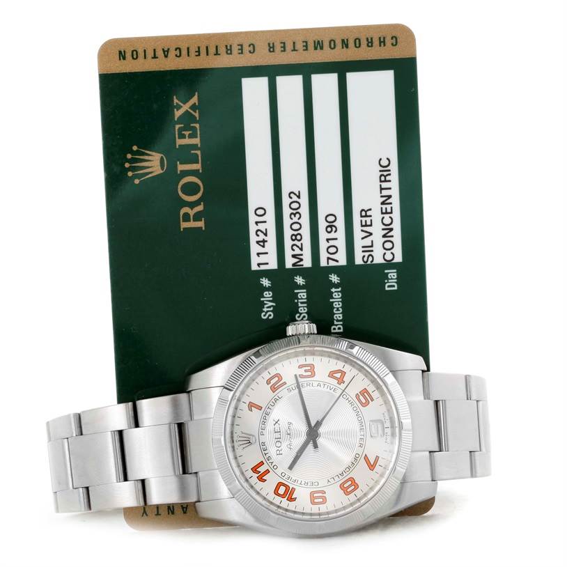 The image shows a Rolex Air-King 114210 Men's Stainless Steel Silver Dial 114210 Men's Stainless Steel Silver Dial watch laying flat with its dial and bracelet visible, along with its certification card.