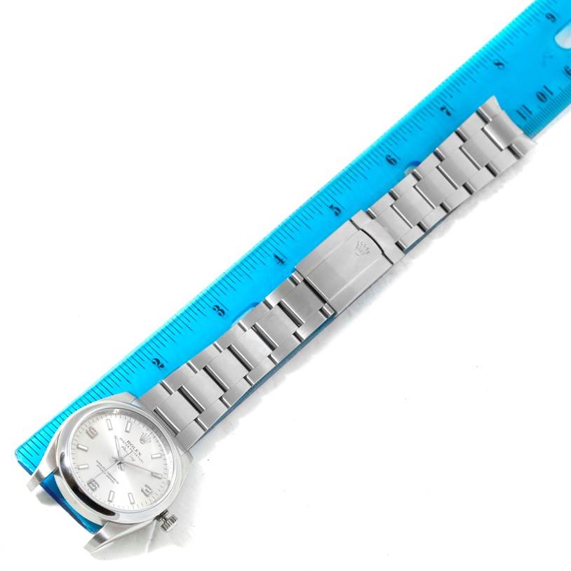 The Rolex Air-King 114200 Men's Stainless Steel Silver Dial 114200 Men's Stainless Steel Silver Dial watch is shown from a top view, displaying the face and full metal bracelet alongside a blue ruler.