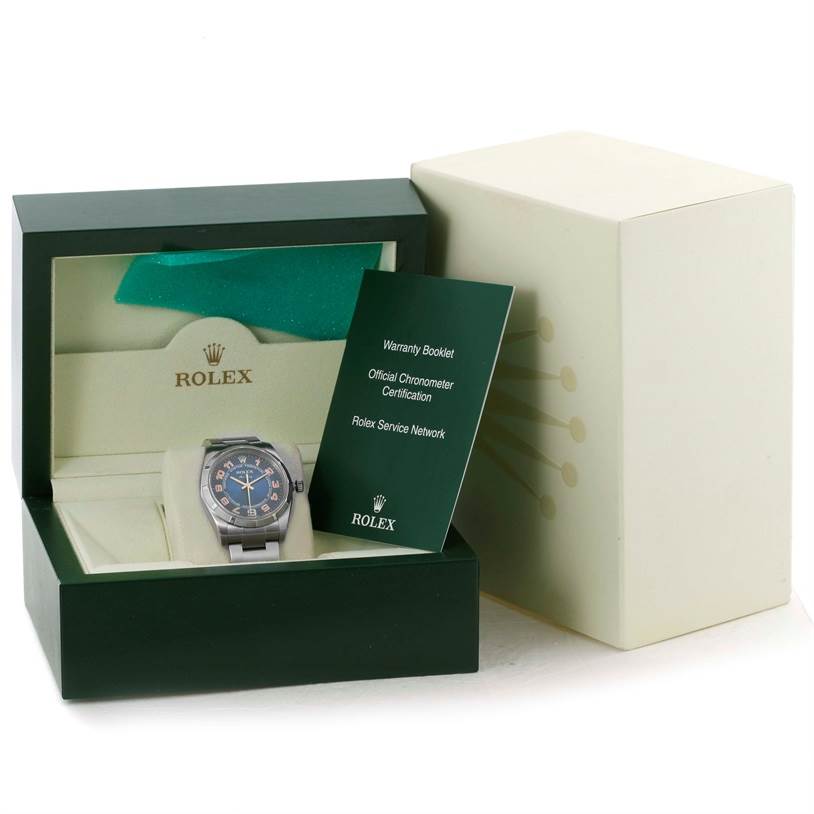 The Rolex Air-King 114210 Men's Stainless Steel Blue Dial 114210 Men's Stainless Steel Blue Dial watch is shown in an open box with warranty booklets displayed beside it.