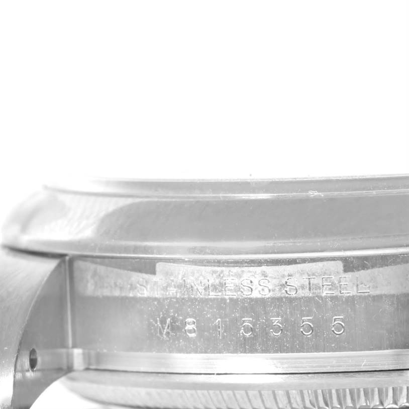 The image shows a close-up side view of a Rolex Air-King 114200 Men
s Stainless Steel Blue Dial 114200 Men
s Stainless Steel Blue Dial watch case, highlighting the stainless steel material and serial number.