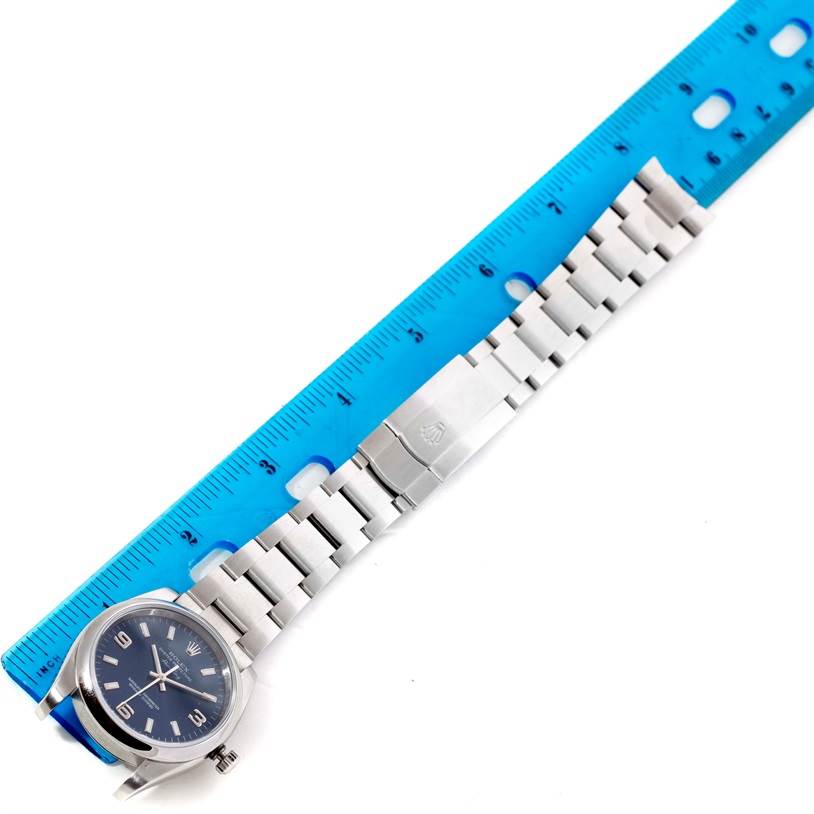 The image shows the entire Rolex Air-King 114200 Men's Stainless Steel Blue Dial 114200 Men's Stainless Steel Blue Dial watch laid flat with a blue ruler beside it, displaying the watch face and metal band.