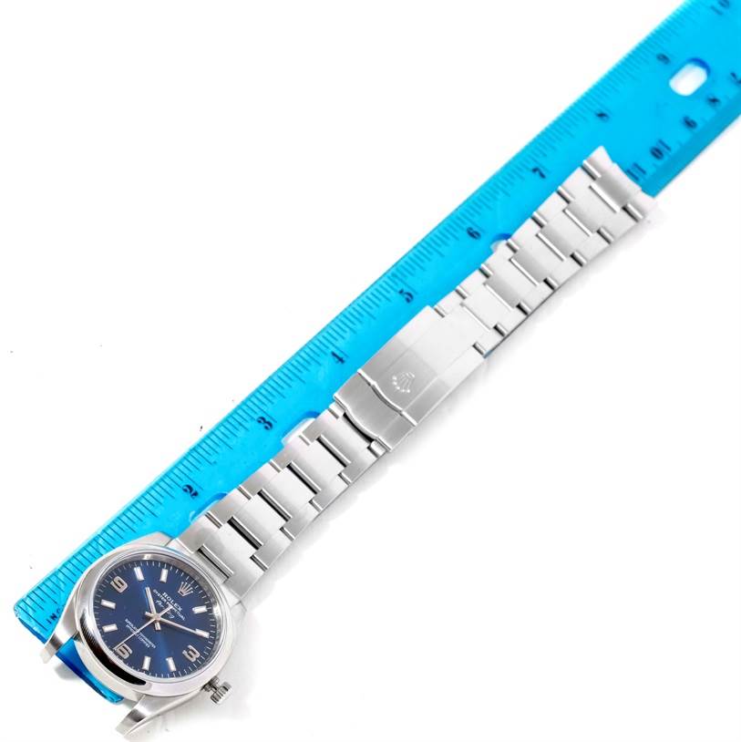 This image shows a full view of the Rolex Air-King 114200 Men's Stainless Steel Blue Dial 114200 Men's Stainless Steel Blue Dial watch laid flat against a ruler, displaying the bracelet and clasp.