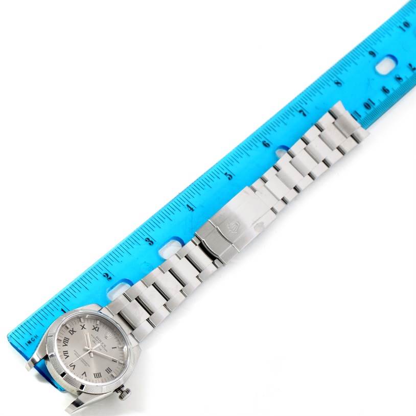 The image shows a Rolex Air-King 114210 Men's Stainless Steel Silver Dial 114210 Men's Stainless Steel Silver Dial watch lying flat beside a blue ruler, highlighting the watch face and metal bracelet.