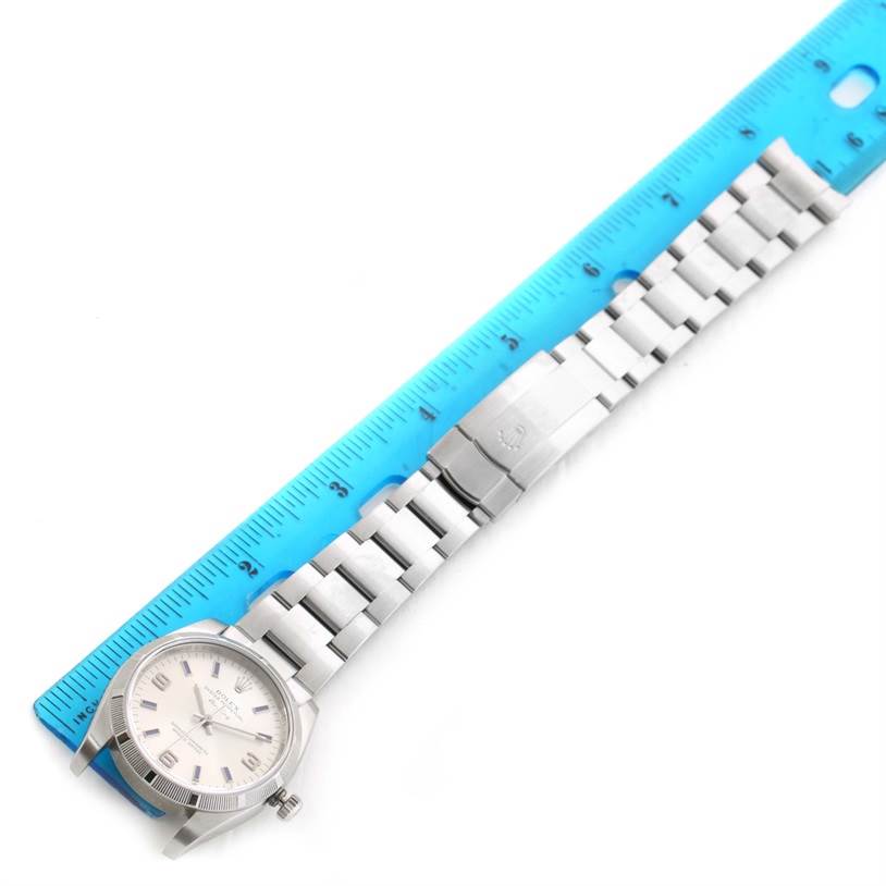 The Rolex Air-King 114210 Men's Stainless Steel Silver Dial 114210 Men's Stainless Steel Silver Dial watch is shown from an overhead angle, including the face, bracelet, and clasp, beside a blue ruler for scale.