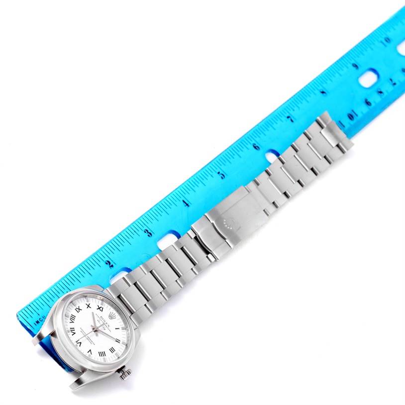 The image shows a top-down view of a Rolex Air-King 114200 Men's Stainless Steel White Dial 114200 Men's Stainless Steel White Dial watch, highlighting its face, bracelet, and clasp next to a blue ruler.