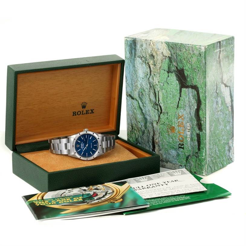 The Rolex Air-King 14010 Men's Stainless Steel Blue Dial 14010 Men's Stainless Steel Blue Dial watch is displayed in an open green box with booklets in front and its outer packaging beside it.