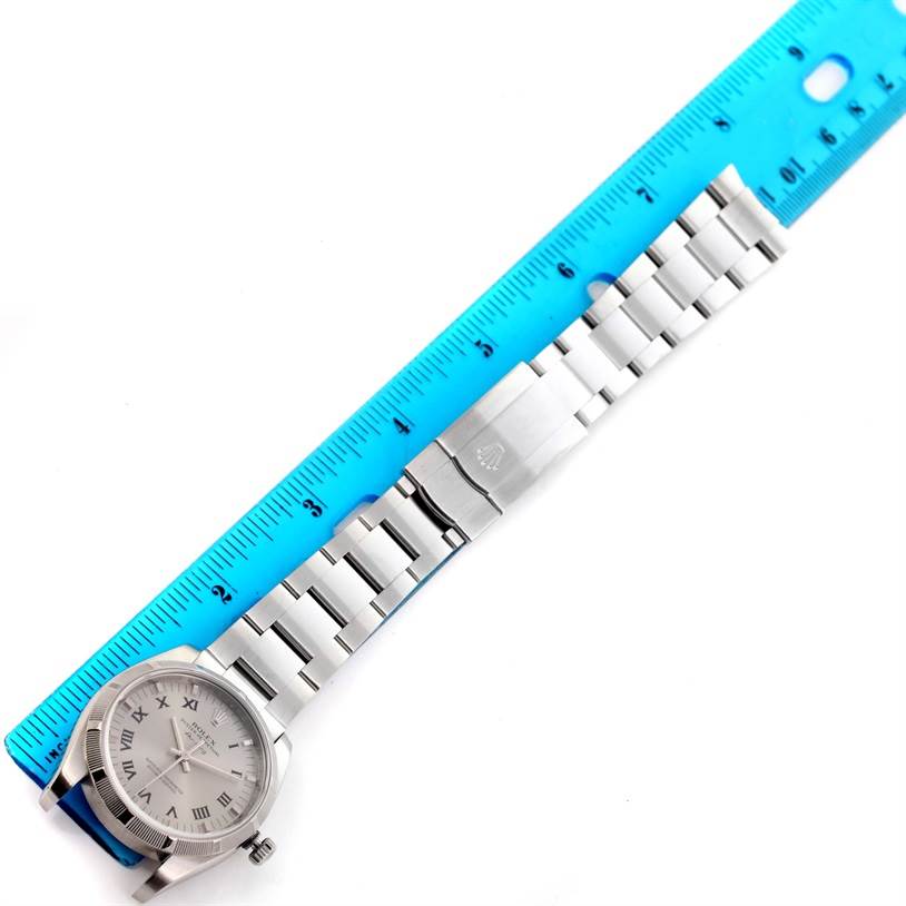 The Rolex Air-King 114210 Men's Stainless Steel Silver Dial 114210 Men's Stainless Steel Silver Dial watch is shown fully extended with its bracelet and clasp, next to a blue ruler for scale.