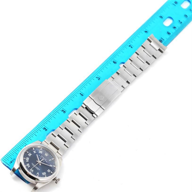 The Rolex Air-King 114200 Men's Stainless Steel Blue Dial 114200 Men's Stainless Steel Blue Dial watch is shown from above, displaying the face, bracelet, and clasp next to a ruler.