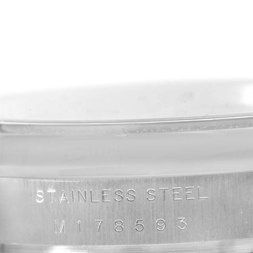 The image shows a close-up of the side view of a Rolex Air-King 114200 Men's Stainless Steel Blue Dial 114200 Men's Stainless Steel Blue Dial watch, with "Stainless Steel" and a serial number engraved.