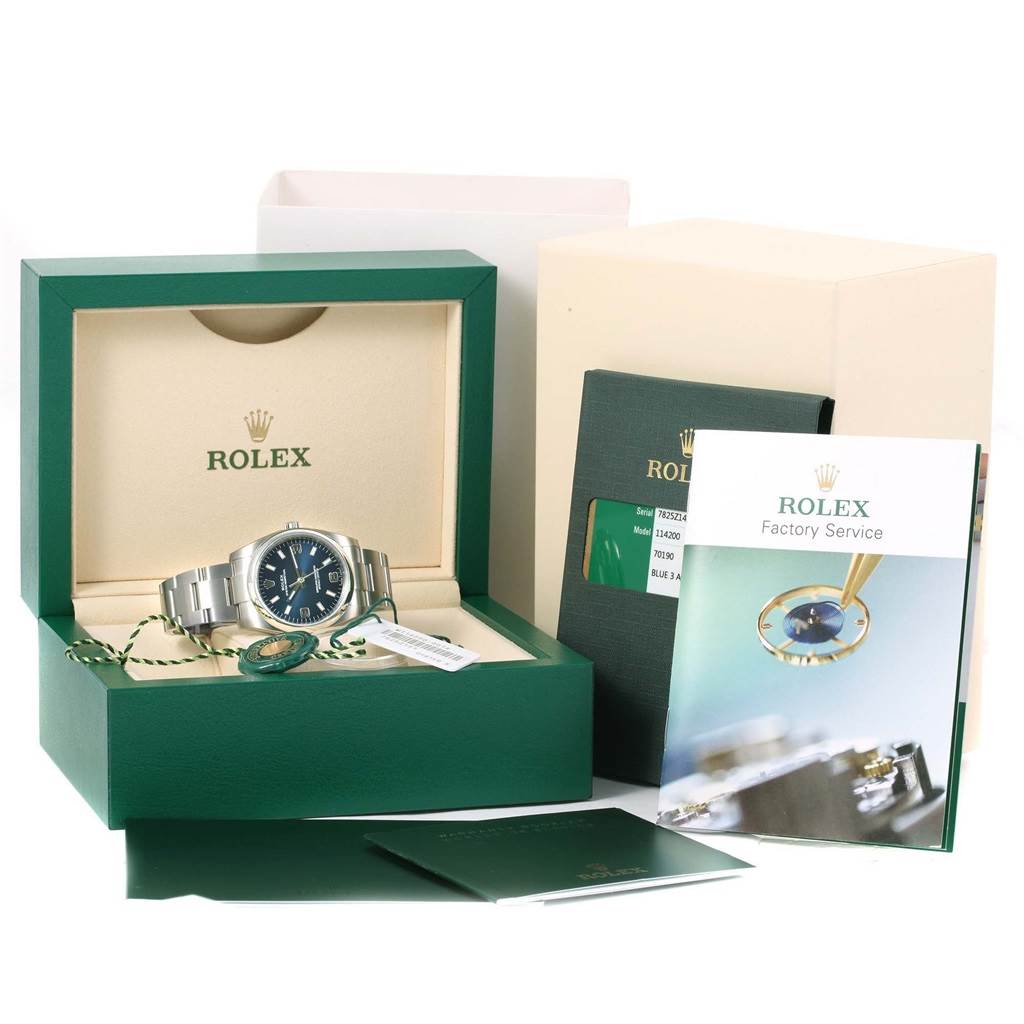 The Rolex Air-King 114200BLASO Men's Stainless Steel Blue Dial 114200BLASO Men's Stainless Steel Blue Dial watch is displayed in its box, accompanied by manuals, booklets, and tags.