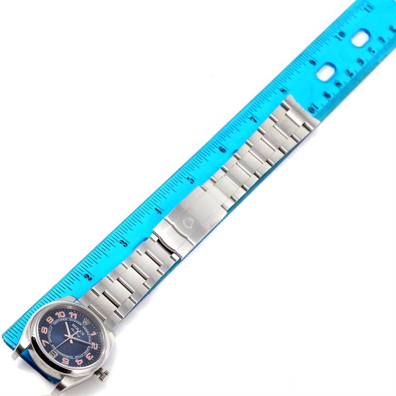 The Rolex Air-King 114200 Men's Stainless Steel Blue Dial 114200 Men's Stainless Steel Blue Dial watch is shown from a top-down angle with its face and entire bracelet next to a blue ruler for scale.