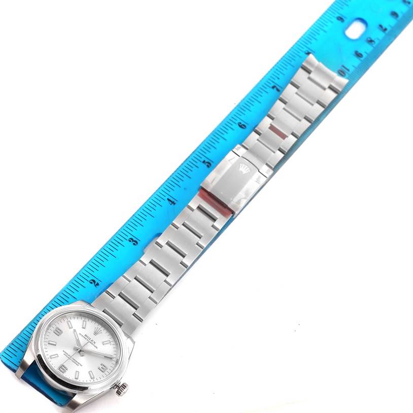 The image displays the Rolex Air-King 114200 Men's Stainless Steel Silver Dial 114200 Men's Stainless Steel Silver Dial watch laid flat, showing its full stainless steel bracelet alongside a blue ruler for measurement.