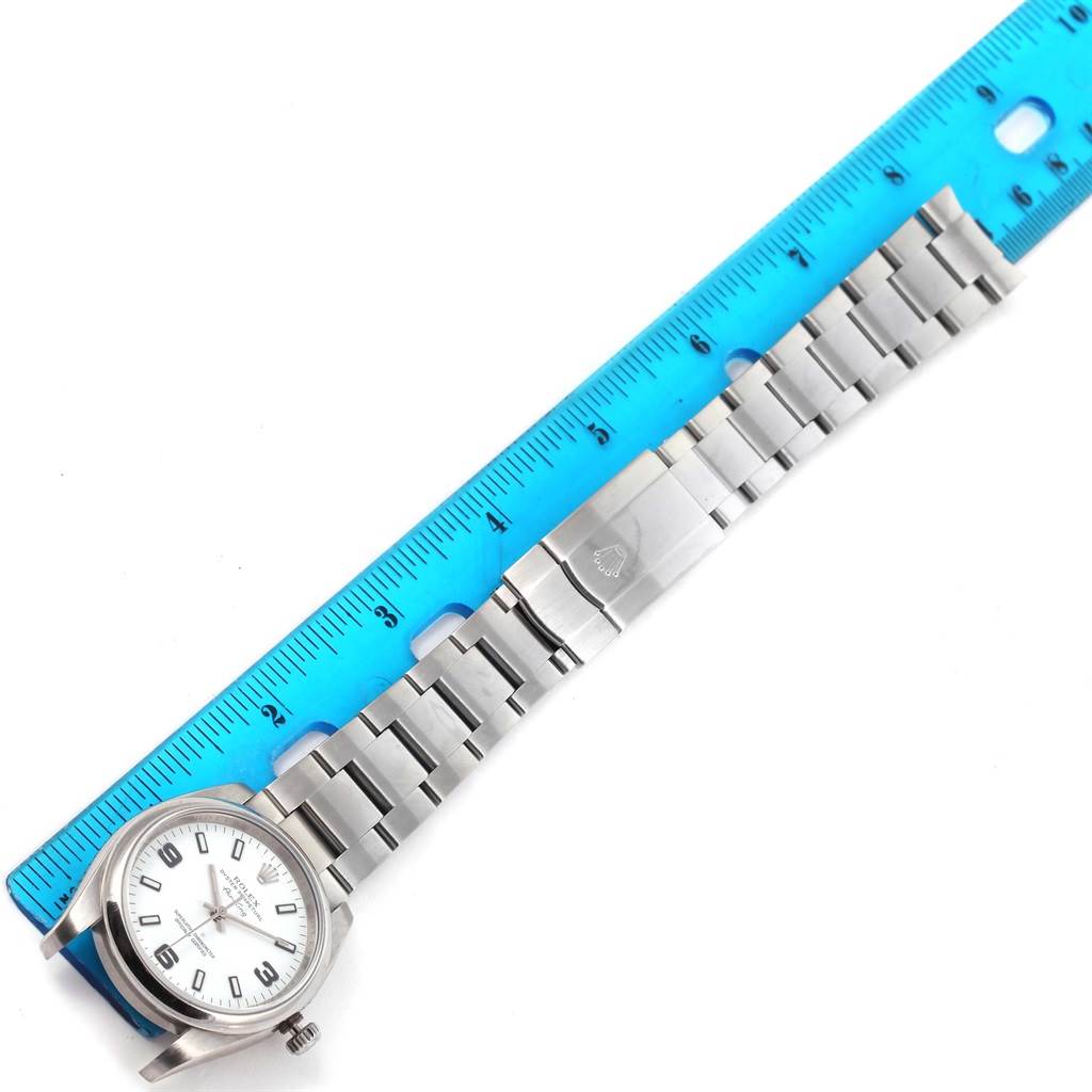 The image shows a top view of a Rolex Air-King 114200 Men's Stainless Steel White Dial 114200 Men's Stainless Steel White Dial watch, including its face, bracelet, and clasp, alongside a blue ruler.