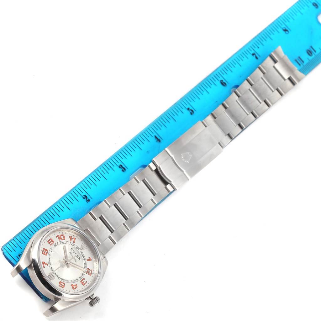 This image shows a top-down view of a Rolex Air-King 114200 Men's Stainless Steel Silver Dial 114200 Men's Stainless Steel Silver Dial watch, including its face and stainless steel bracelet, next to a blue ruler.