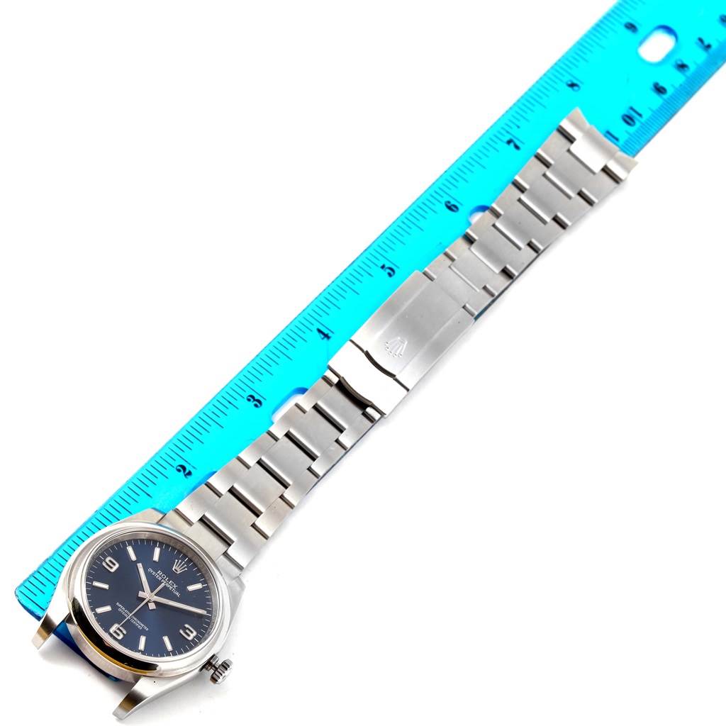 The image shows a Rolex Air-King 116000 Men's Stainless Steel Blue Dial 116000 Men's Stainless Steel Blue Dial watch lying flat with a blue ruler to the right, highlighting its full bracelet length.
