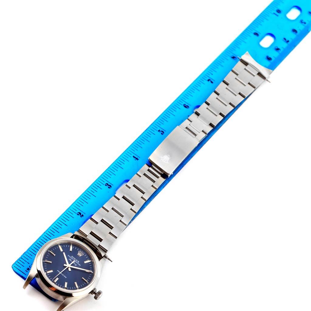 The Rolex Air-King 14000 Men's Stainless Steel Black Dial 14000 Men's Stainless Steel Black Dial watch is shown at a top-down angle, displaying its dial, bracelet, and clasp next to a blue ruler for scale.