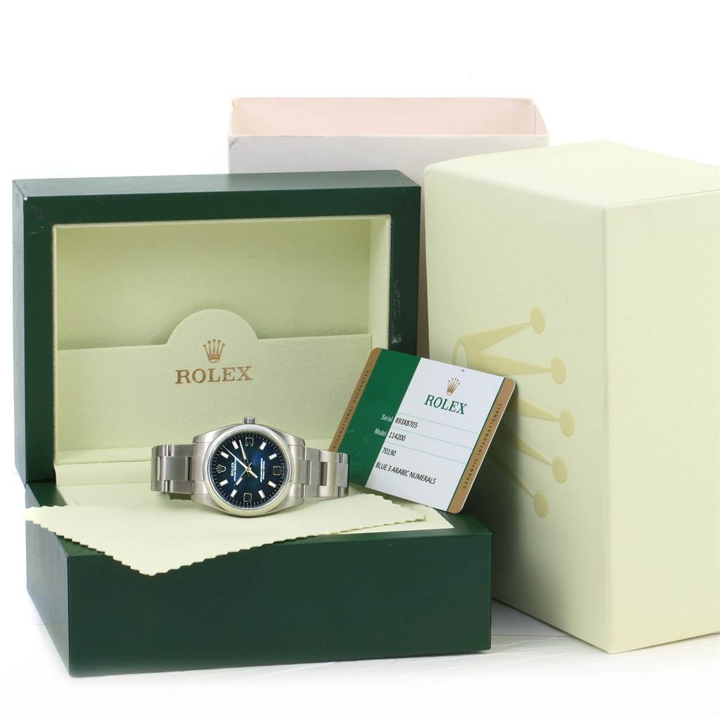 The Rolex Air-King 114200 Men's Stainless Steel Blue Dial 114200 Men's Stainless Steel Blue Dial watch is shown from the front inside its open box, with its warranty card and outer packaging visible.