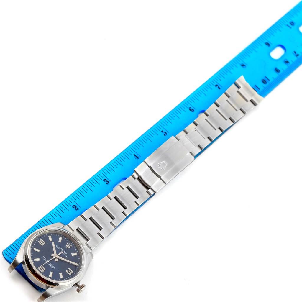 This image shows a top view of a Rolex Air-King 114200 Men's Stainless Steel Blue Dial 114200 Men's Stainless Steel Blue Dial watch, displaying its face, bezel, and stainless steel bracelet with a measuring ruler beside it.