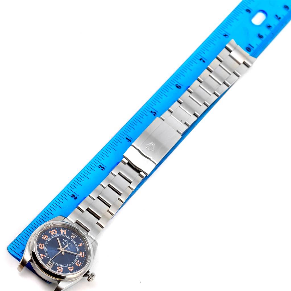 The image shows the Rolex Air-King 114200 Men's Stainless Steel Blue Dial 114200 Men's Stainless Steel Blue Dial watch lying flat with its face and bracelet fully visible, measured against a blue ruler.