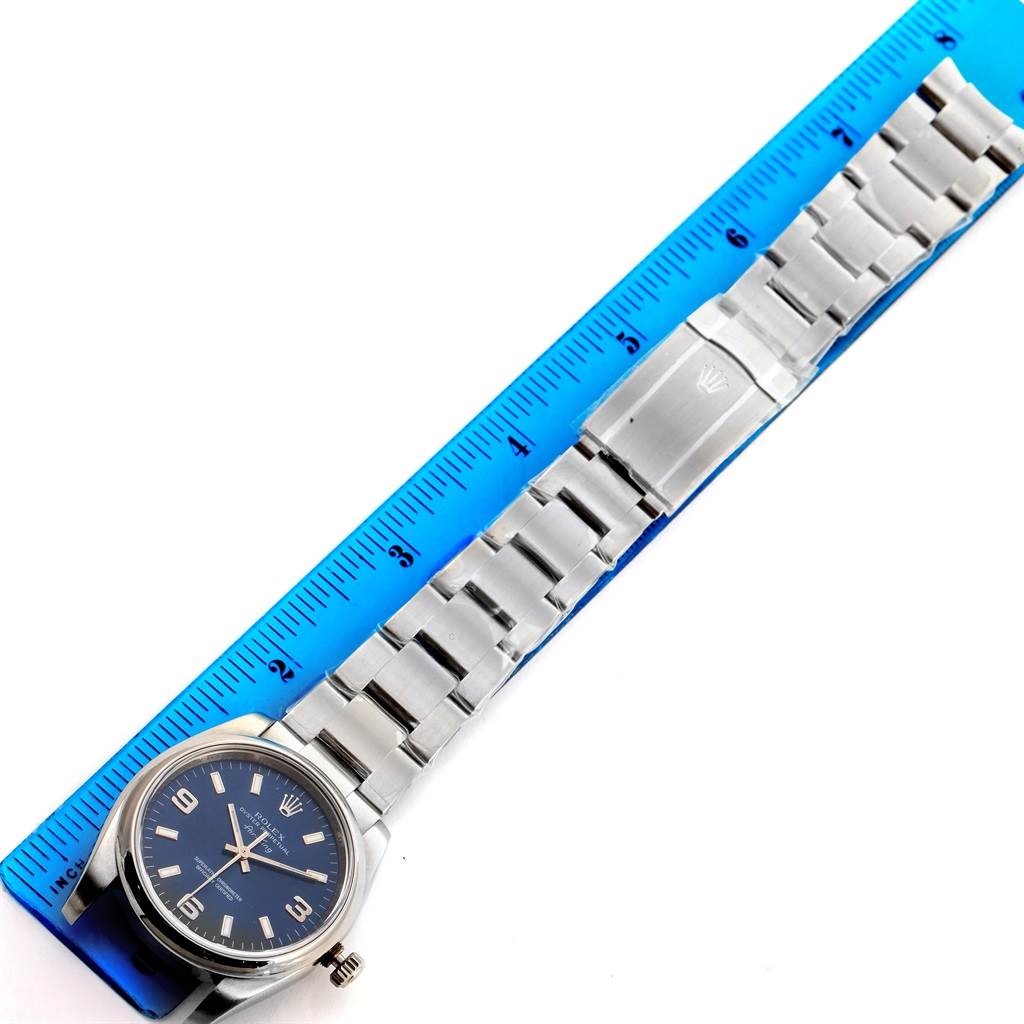 The image shows a Rolex Air-King 114200BLASO Men's Stainless Steel Blue Dial 114200BLASO Men's Stainless Steel Blue Dial watch laid flat with a blue ruler for measurement, capturing the watch face, bracelet, and clasp.